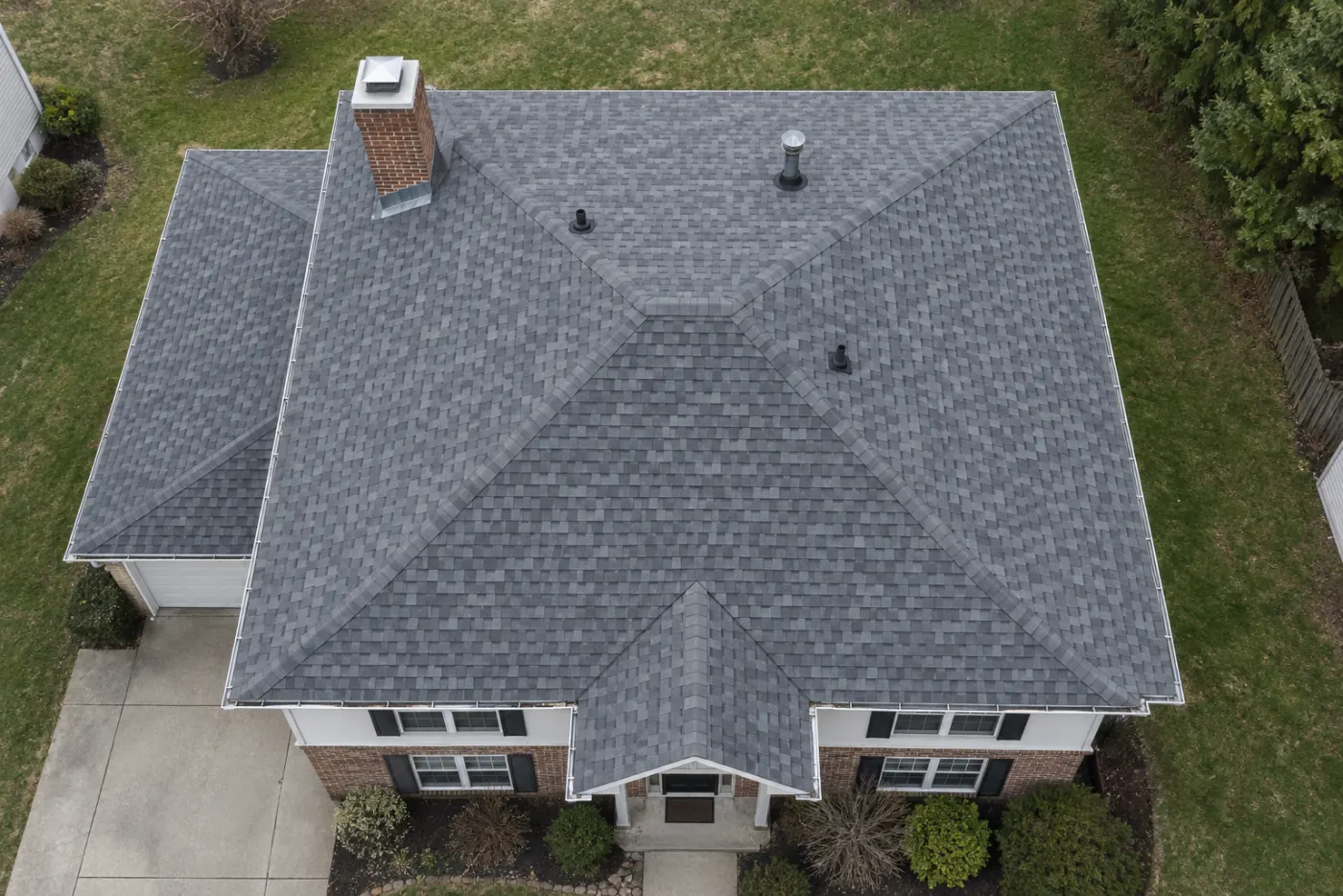 Top-down view of a suburban home roof showing gray architectural shingles, a brick chimney with flashing, valleys, and vent boots