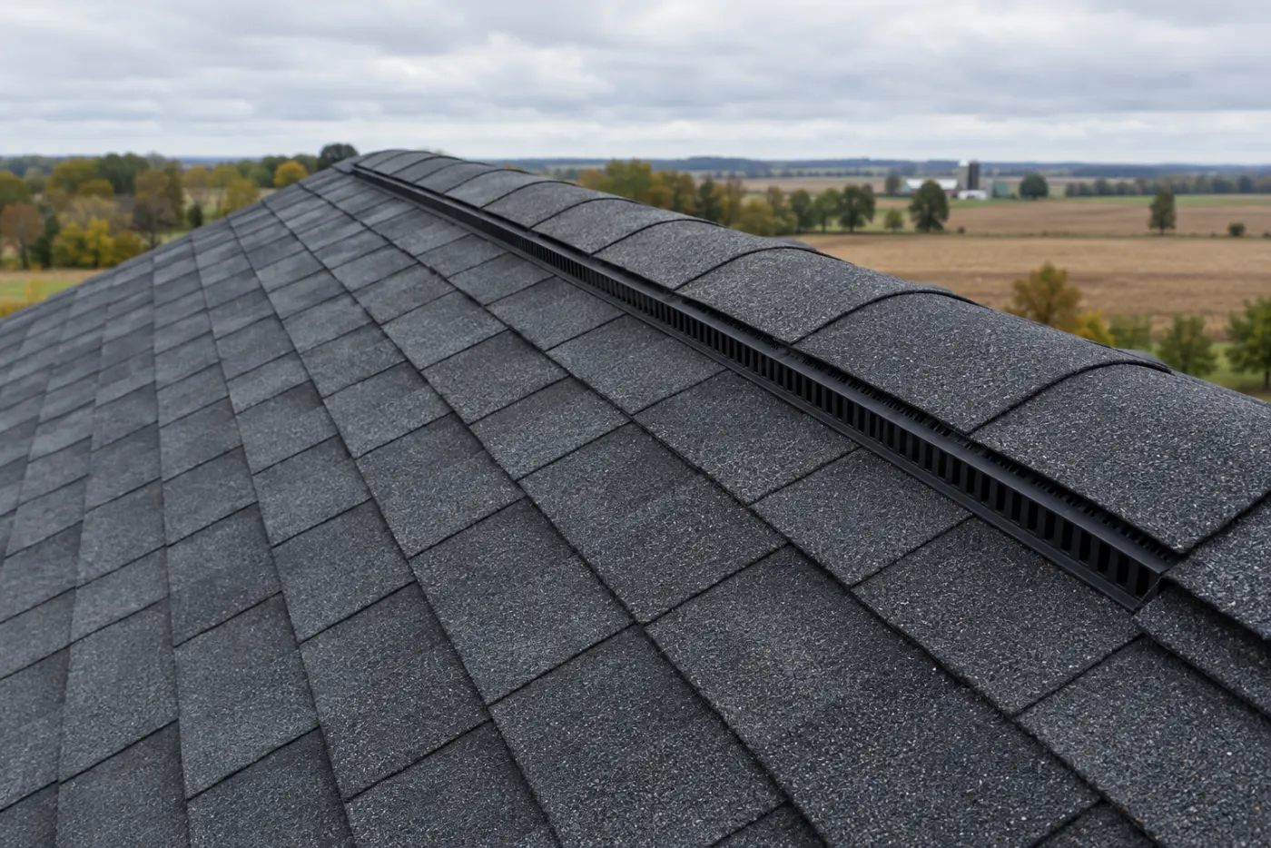 Close-up of new charcoal architectural asphalt shingles and a ridge vent on a residential roof with Ohio farmland behind